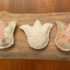 May include: Three handmade fabric tulips in different patterns. The first tulip is white with a quilted design. The second tulip is green with a pink and white floral pattern. The third tulip is white with a pink and white gingham pattern.