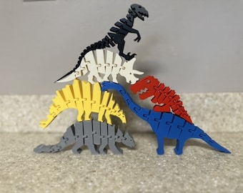 May include: A collection of colorful wooden dinosaur puzzles. The dinosaurs are in various colors, including black, white, yellow, gray, red, and blue. The puzzles are assembled and stacked, showcasing the different dinosaur species.