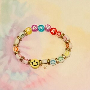 May include: A colorful beaded bracelet with the word "KARMA" spelled out in white letters on the beads. The beads are a mix of rainbow colors and smiley faces.