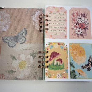 May include: Open journal with a spiral binding. The left page features a butterfly and floral design. The right page has decorative tags with floral illustrations and the text "Someone told me there's a girl out there with love in her eyes and flowers in her hair."