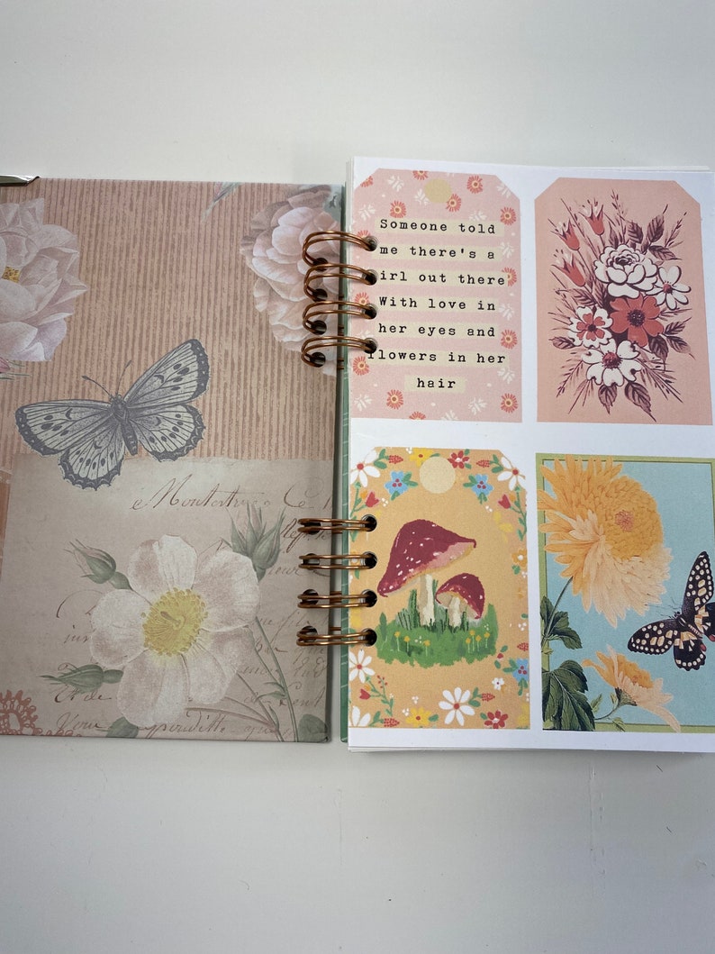 May include: Open journal with a spiral binding. The left page features a butterfly and floral design. The right page has decorative tags with floral illustrations and the text "Someone told me there's a girl out there with love in her eyes and flowers in her hair."