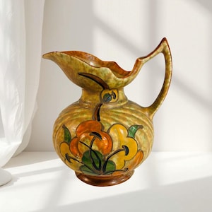 May include: A vintage ceramic jug with a bulbous body and a curved handle. The jug features a floral design in orange, yellow, and green against a tan background. The jug has a spout and is approximately 20 cm tall.