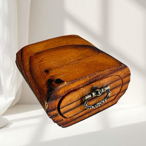 Pode incluir: Uma pequena caixa de madeira com uma gaveta. A caixa é tingida com uma cor castanha quente e tem um topo curvo. A gaveta tem uma pega decorativa de metal. A caixa parece ser feita de várias peças de madeira.