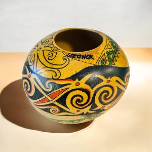 May include: A spherical, hand-painted gourd with a wide opening. The gourd has a yellow base with black, orange, and green tribal patterns. The word "Sarawak" is written on the side. The gourd is likely used for decorative purposes.