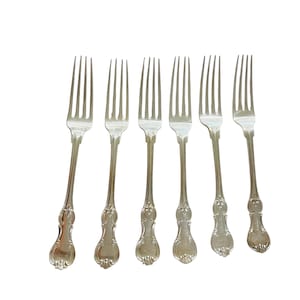 Peut inclure: Six fourchettes argentées avec des manches ornés sont présentées sur fond blanc. Chaque fourchette a trois dents et des détails décoratifs. La coutellerie est probablement pour les repas formels, mesurant environ 20 cm de long.