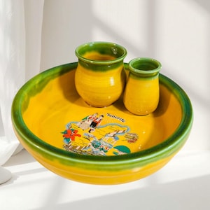 Può includere: Un set in ceramica giallo e verde composto da una ciotola grande e due tazze più piccole. La ciotola presenta una colorata illustrazione grafica di Tenerife con il testo "Tenerife" stampato in nero. I pezzi hanno una finitura smaltata.