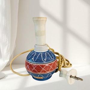 May include: A ceramic lamp base with a blue and red geometric design. The base has a white neck and a tan electrical cord with a white plug. The lamp is designed to hold a light bulb.