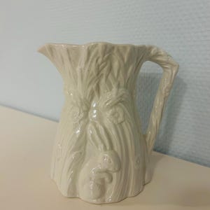 Könnte beinhalten: Eine weiße Keramik-Tasse mit schwarzem Henkel und dem Text "But First, Coffee" in schwarzer, handschriftlicher Schrift. Die Tasse steht auf einer weißen Oberfläche.