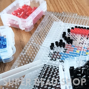 May include: A close-up of a clear plastic bead organizer with red, black, and blue beads. The organizer has multiple compartments and is labeled "SUPERBEADSHOP".