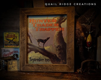 May include: A vintage framed print of a hunting magazine cover featuring a black and brown dog on a tree branch. The magazine is titled "Hunter Trader Trapper" and the date is September 1919. The text "20 cents" is also visible.