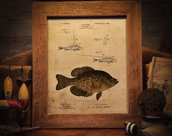 Pode incluir: Uma ilustração vintage de um peixe crappie preto, com o texto "The Black Crappie" abaixo da imagem. A ilustração é de uma patente para um anzol de pesca, com o número da patente e a data visíveis. A imagem está emoldurada em uma moldura de madeira.