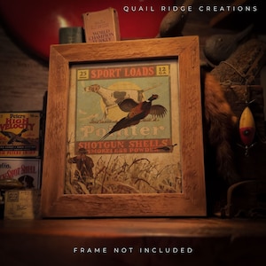 May include: A framed vintage print with a hunting theme. The print features a pheasant in flight, a hunting dog, and the words "Sport Loads" and "Shotgun Shells." The frame is made of light brown wood. The text "FRAME NOT INCLUDED" is at the bottom.