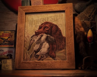 May include: A vintage print of a brown and white dog holding a duck in its mouth. The print is framed in a rustic wooden frame. The text "The Celebrated Winchester Repeating Rifles" is printed on the print.