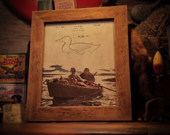 May include: A vintage framed print of a duck decoy patent drawing. The drawing shows a side view of the decoy with the text "Fig. 1." The print also includes a black and white illustration of two people in a boat on a lake. The text "July 2, 1941. A. H. OLSEN NORTH ST. PAUL, MINN. Filed Feb. 12, 1940. 2,247,450" is printed below the drawing. The frame is not included.