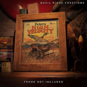 May include: A vintage framed print of a Peters High Velocity 16 GA. shotgun shell advertisement. The print features a hunter aiming a shotgun at a flying duck with the text "Peters High Velocity Rustless" in a yellow banner.