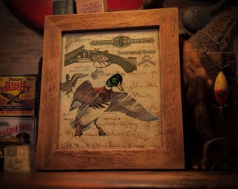 May include: A framed print with a vintage aesthetic. The artwork features a detailed illustration of a mallard duck in flight, with a shotgun and text from Duchame, Fletcher & Co. The wooden frame adds a rustic touch. Text at the bottom reads "FRAME NOT INCLUDED".