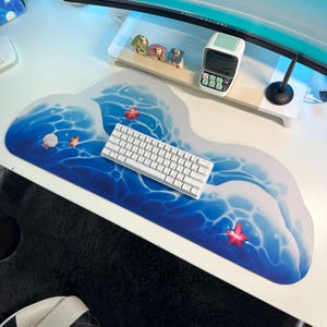 Peut inclure: Un tapis de bureau en forme de vague bleu et blanc avec un clavier blanc et des motifs d'étoiles de mer rouges.