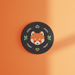 May include: Black and white round coaster with a red panda face in the centre. The coaster has a green and white floral design around the edge.