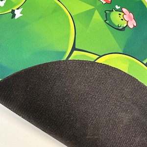 May include: A green and black gaming mouse pad with a cartoon character design. The mouse pad has a black rubberized underside.