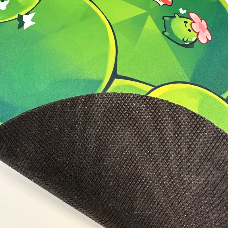 May include: A green and black gaming mouse pad with a cartoon character design. The mouse pad has a black rubberized underside.