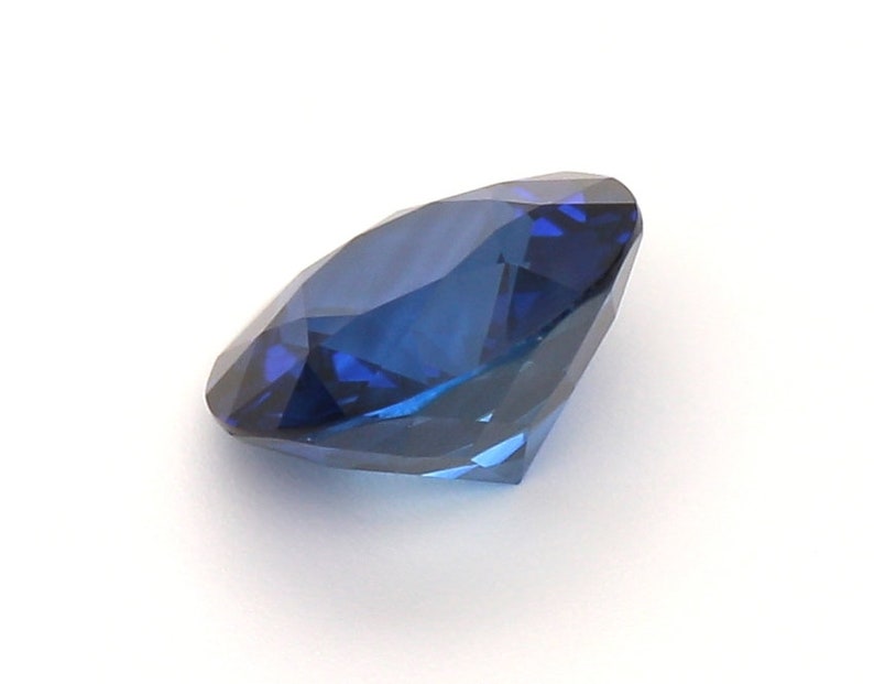 May include: A deep blue sapphire gemstone with a round cut and many facets.