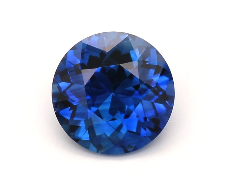 May include: A round, deep blue sapphire gemstone with a faceted cut.
