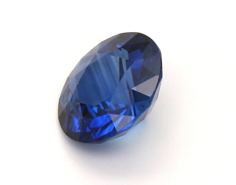 May include: A deep blue sapphire gemstone with a round cut and a faceted design.