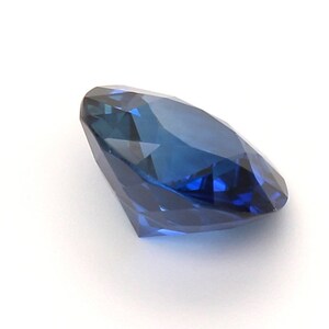 May include: A deep blue sapphire gemstone with a round brilliant cut. The gemstone is faceted and has a high degree of brilliance.