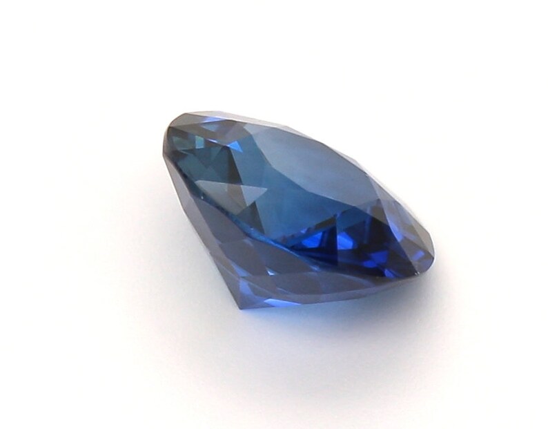 May include: A deep blue sapphire gemstone with a round brilliant cut. The gemstone is faceted and has a high degree of brilliance.