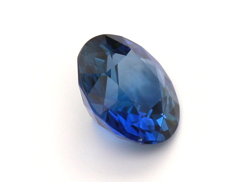 May include: A deep blue oval sapphire gemstone with a faceted cut.
