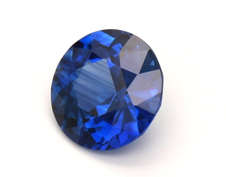 May include: A deep blue sapphire gemstone with a round cut and a faceted design.