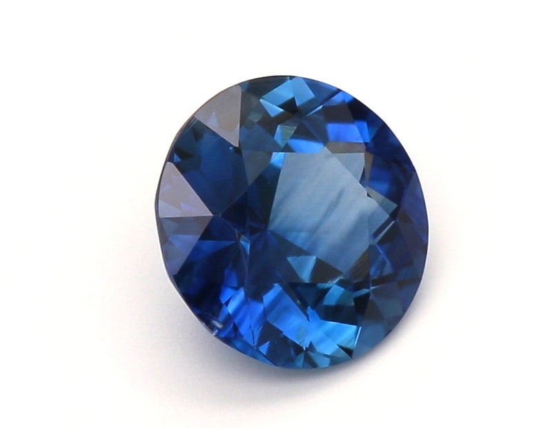 May include: A deep blue sapphire gemstone with a round cut and a faceted design.
