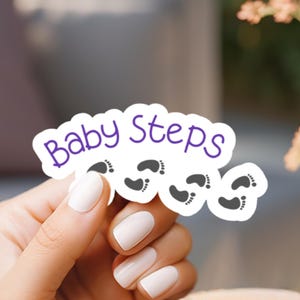 May include: A white sticker with the text "Baby Steps" in purple lettering and several gray footprints.