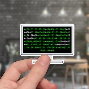 May include: A sticker of a computer monitor with a white border. The screen displays green binary code. The sticker is held by a hand, with a blurred background of a room with a brick wall and wooden furniture.