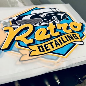 Może przedstawiać: Logo w kolorze ż&oacute;łtym i niebieskim z tekstem "Retro Detailing" i ilustracją czarno-białego samochodu vintage.