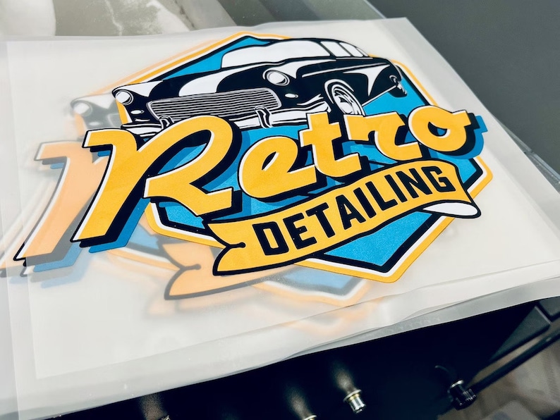 Może przedstawiać: Logo w kolorze ż&oacute;łtym i niebieskim z tekstem "Retro Detailing" i ilustracją czarno-białego samochodu vintage.
