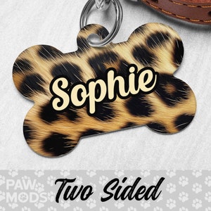 May include: A bone-shaped dog tag with a leopard print design. The tag has the name "Sophie" written in a yellow font. The tag is two-sided.