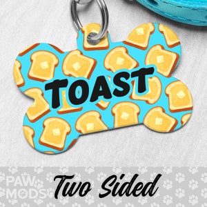 May include: A blue bone-shaped dog tag with a white and yellow pattern of toast. The tag has the word "TOAST" printed in black letters. The tag is two-sided.