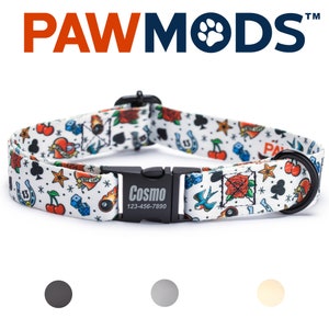 May include: A white dog collar with a colorful tattoo-themed print featuring cherries, dice, playing cards, a horseshoe, a heart, a rose, a bird, and a skull. The collar has a black buckle with the text "Cosmo" and a phone number.