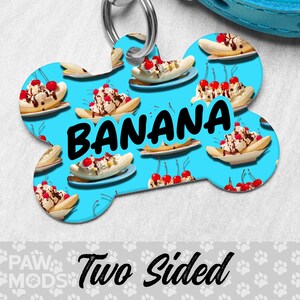 May include: A two-sided, bone-shaped pet tag with a light blue background. The tag features a repeating pattern of banana splits and the word "BANANA" in large black letters. The tag also says "Two Sided".