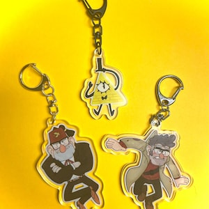May include: Three acrylic keychains featuring cartoon characters. One keychain depicts a yellow triangle with a top hat and one eye. The other two keychains show cartoon characters in various poses. Each keychain has a silver-colored chain and clasp.