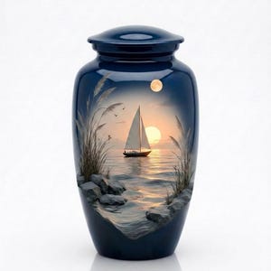 Op de afbeelding: Marineblauwe crematie-urn met een sereen zeelandschapontwerp. Het kunstwerk toont een zeilboot op kalm water bij zonsondergang, met een volle maan en hoge grasaccenten. De urn heeft een bijpassende deksel.