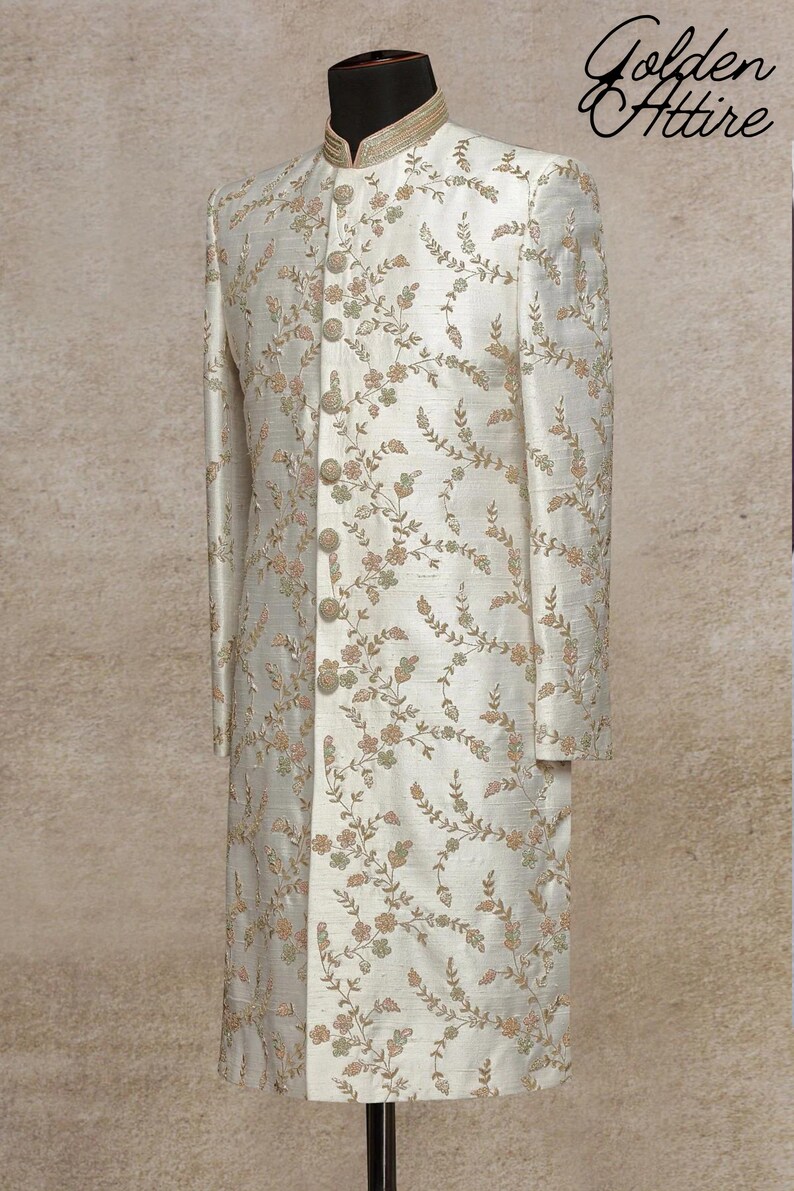 K&ouml;nnte beinhalten: Ein wei&szlig;es, lang&auml;rmliges Kleidungsst&uuml;ck mit einem Stehkragen und floralen Stickereien. Das Kleidungsst&uuml;ck hat eine Knopfleiste vorne und befindet sich auf einer Schaufensterpuppe.