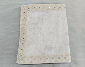 May include: A white fabric square with a decorative border of small mirrors and beads. The fabric has a subtle pattern of small white dots.