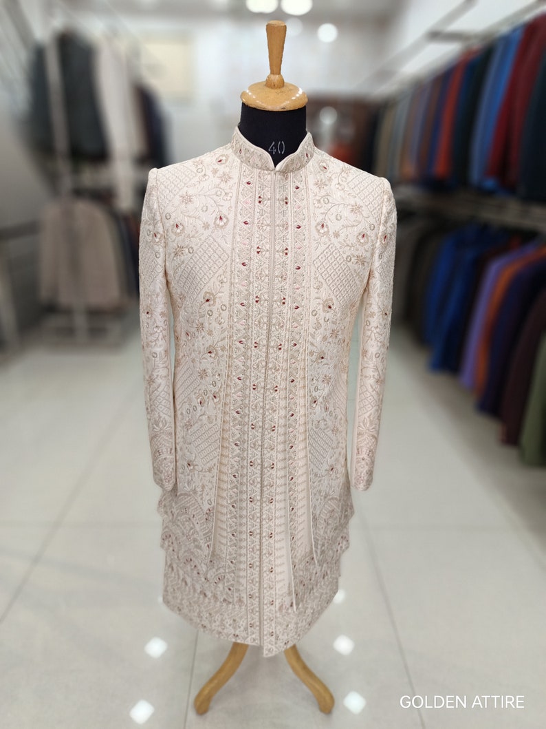 Puede incluir: Una kurta de hombre blanca bordada con cuello alto y adornos rojos. La kurta est&aacute; en un maniqu&iacute; y tiene un dise&ntilde;o tradicional indio.