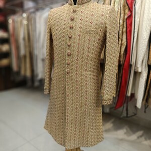May include: A gold embroidered men's sherwani with a pink button closure. The sherwani features a traditional Indian design and is ideal for a wedding or other special occasion.