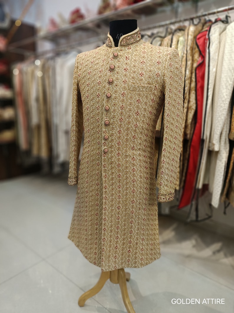 May include: A gold embroidered men's sherwani with a pink button closure. The sherwani features a traditional Indian design and is ideal for a wedding or other special occasion.