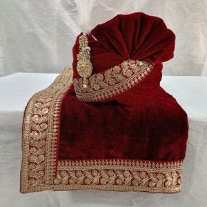 May include: A maroon velvet turban with gold embroidery and a decorative gold ornament. The turban is accompanied by a matching maroon velvet scarf with gold embroidery.