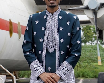May include: A man wearing a dark blue jacket with white embroidery. The jacket has a mandarin collar and long sleeves. The man is standing in front of a white airplane.