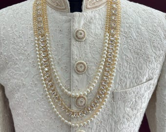 Può includere: Una collana di perle bianche e strass con una catena dorata. La collana è composta da tre file di perle e una fila di strass.